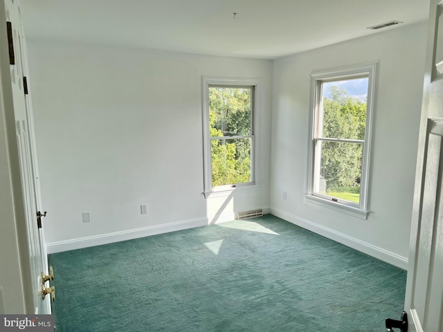 spare room with a healthy amount of sunlight, visible vents, dark carpet, and baseboards