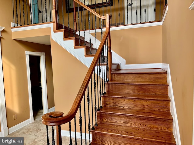 stairs featuring stone finish floor, a towering ceiling, and baseboards