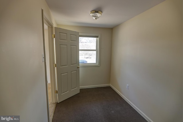 empty room featuring baseboards and dark colored carpet