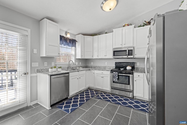 kitchen featuring light stone countertops, white cabinetry, stainless steel appliances, and a sink