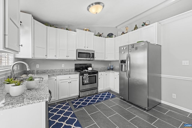 kitchen with light stone counters, stainless steel appliances, white cabinetry, vaulted ceiling, and a sink