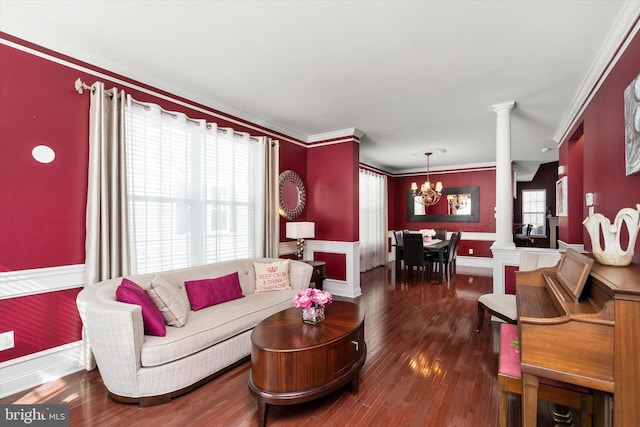 living area featuring a chandelier, dark wood finished floors, crown molding, and decorative columns