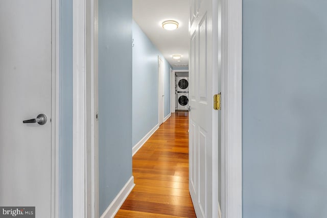 hallway with stacked washer and dryer, light wood-type flooring, and baseboards