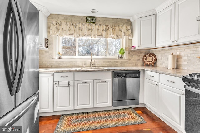 kitchen with decorative backsplash, white cabinets, appliances with stainless steel finishes, dark wood-type flooring, and a sink