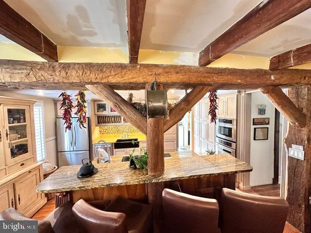 kitchen featuring stainless steel appliances, beam ceiling, light stone counters, and a kitchen breakfast bar