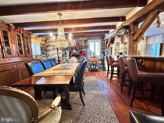 dining area featuring wooden walls, dark wood finished floors, beam ceiling, and an inviting chandelier