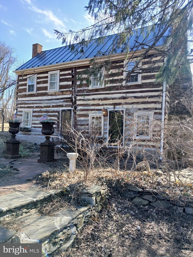 rear view of house with a standing seam roof, a chimney, log siding, and metal roof