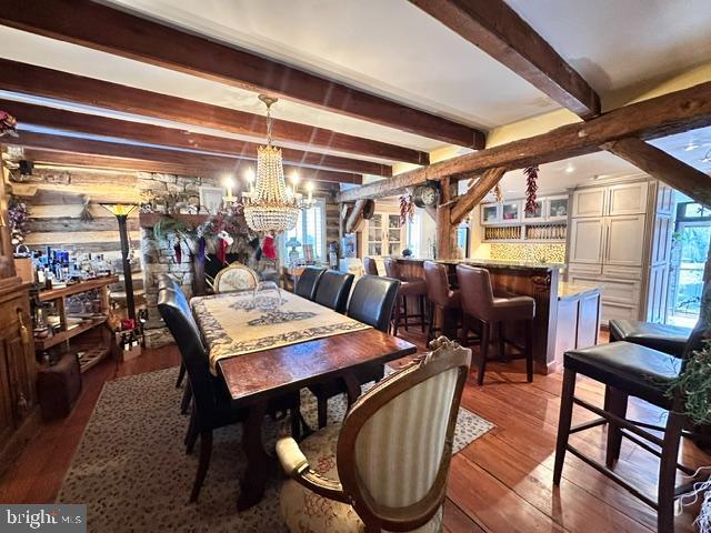 dining space featuring a bar, an inviting chandelier, hardwood / wood-style floors, and beamed ceiling