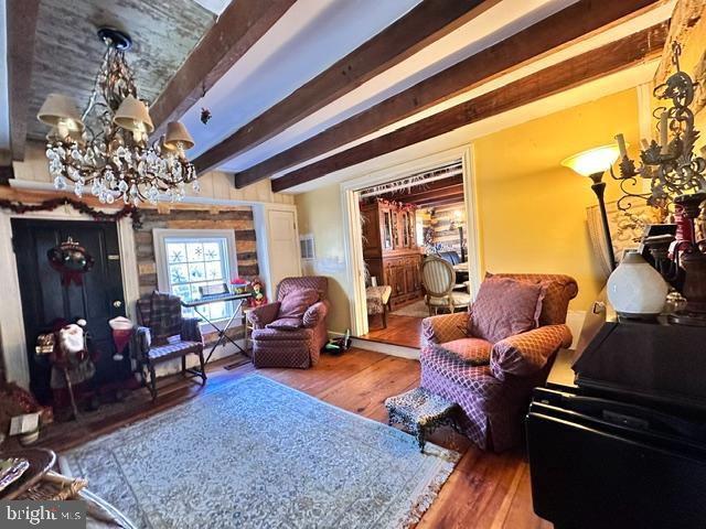 living area with an inviting chandelier, beam ceiling, and wood finished floors