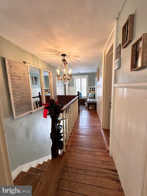 corridor with wood-type flooring, a notable chandelier, and an upstairs landing