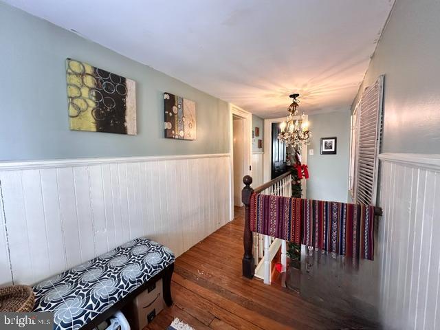 hallway with a wainscoted wall, a chandelier, and wood finished floors