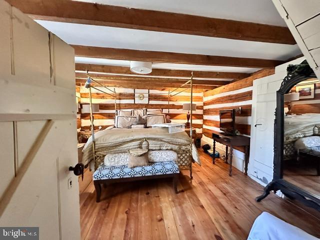 unfurnished bedroom featuring wood walls, beam ceiling, and light wood-style floors