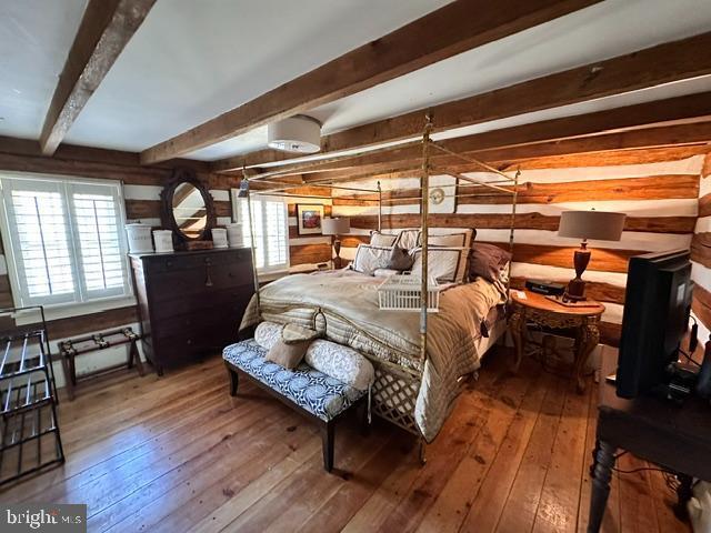 bedroom featuring wood-type flooring, beam ceiling, and wooden walls