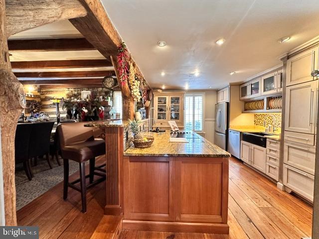 kitchen featuring light wood-style flooring, glass insert cabinets, a peninsula, stainless steel appliances, and stone counters