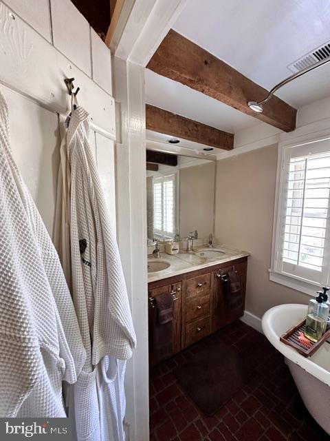 bathroom featuring double vanity, visible vents, beamed ceiling, brick floor, and a sink