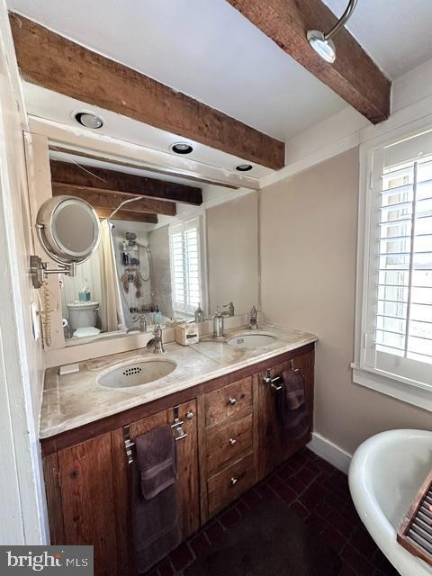 bathroom featuring double vanity, a sink, beam ceiling, and baseboards