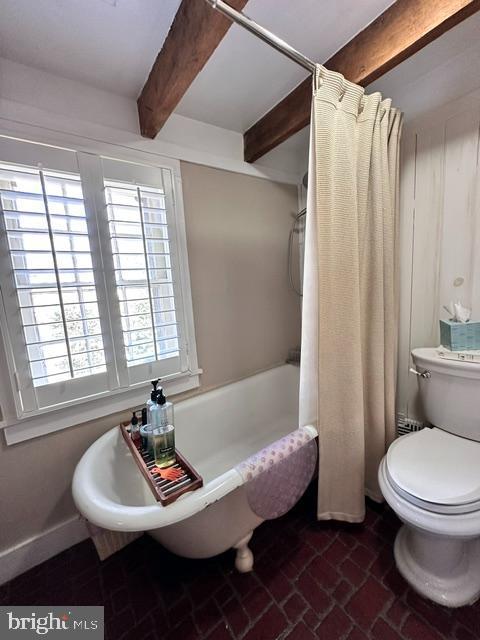 full bathroom with brick floor, toilet, beamed ceiling, and baseboards