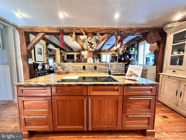 kitchen featuring light wood finished floors, black electric stovetop, glass insert cabinets, brown cabinetry, and light stone countertops