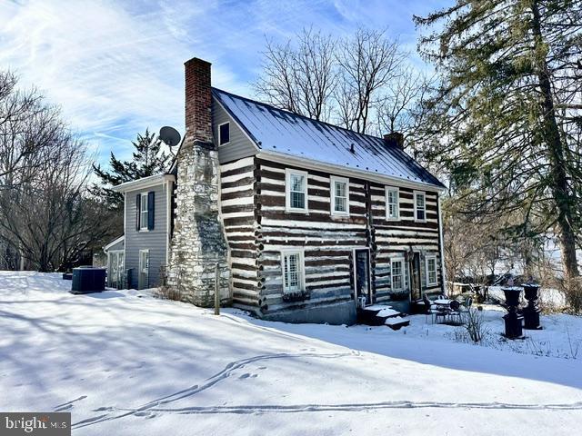 view of front facade featuring a chimney, a standing seam roof, central AC, metal roof, and log exterior