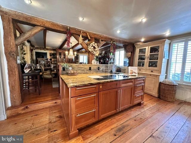 kitchen featuring glass insert cabinets, brown cabinets, a center island, light stone countertops, and light wood-type flooring