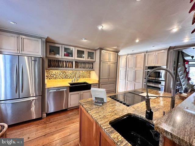 kitchen featuring backsplash, appliances with stainless steel finishes, light wood-style floors, glass insert cabinets, and a sink