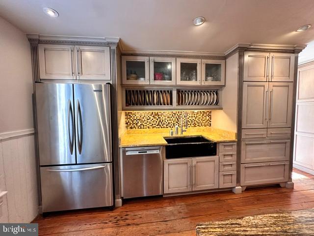 kitchen with hardwood / wood-style flooring, a wainscoted wall, a sink, appliances with stainless steel finishes, and glass insert cabinets