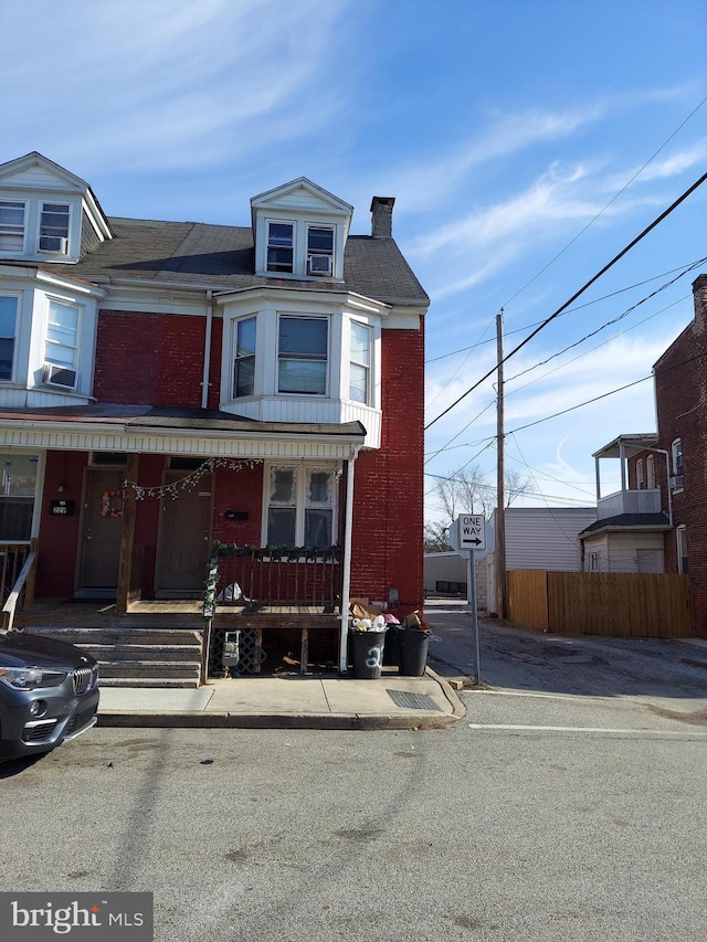 multi unit property featuring a chimney, fence, a porch, and brick siding