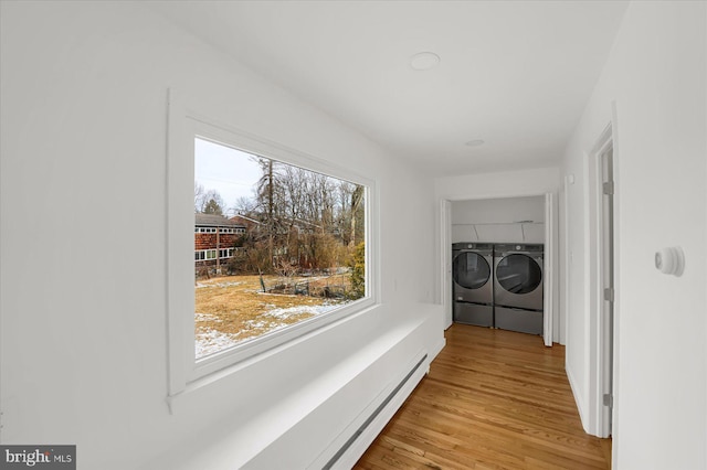 clothes washing area featuring a baseboard heating unit, laundry area, light wood-style flooring, and washer and dryer