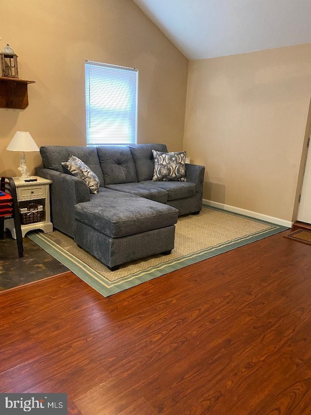 living room featuring vaulted ceiling, baseboards, and wood finished floors