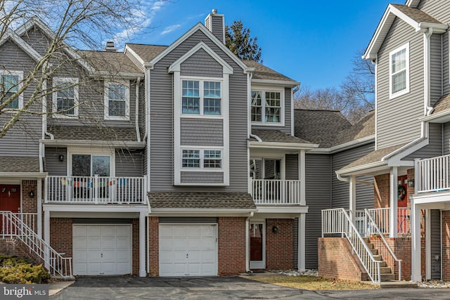 multi unit property featuring driveway, brick siding, roof with shingles, and a chimney