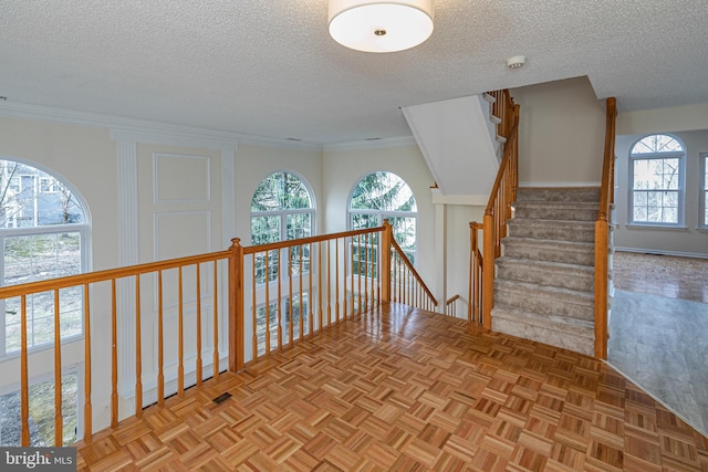 hallway with a healthy amount of sunlight, ornamental molding, and a textured ceiling