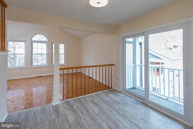 spare room with parquet flooring, baseboards, vaulted ceiling, and a textured ceiling