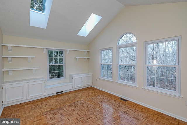 empty room featuring a skylight, baseboards, visible vents, and high vaulted ceiling