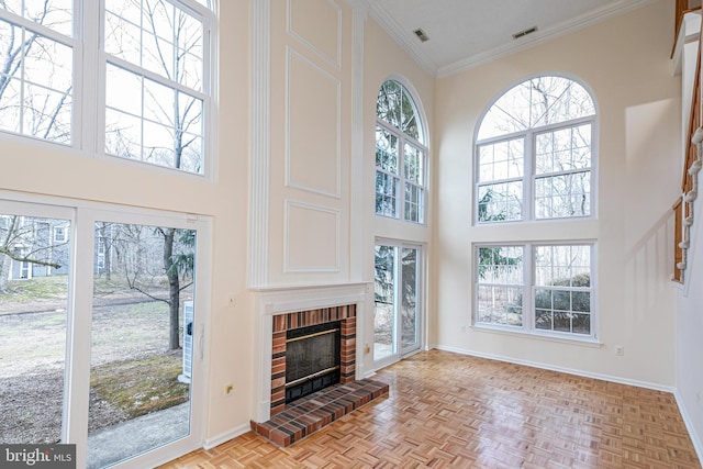 living room with baseboards, visible vents, a high ceiling, crown molding, and a fireplace