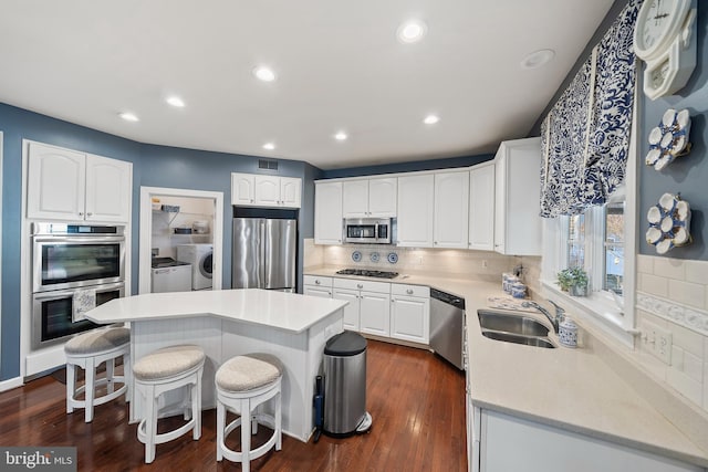 kitchen featuring visible vents, appliances with stainless steel finishes, a kitchen breakfast bar, washing machine and dryer, and white cabinetry