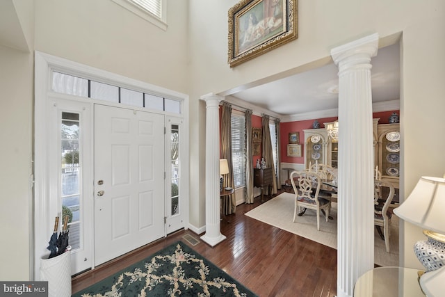 foyer with crown molding, a healthy amount of sunlight, dark wood-type flooring, and ornate columns