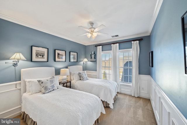 bedroom with ceiling fan, light colored carpet, visible vents, ornamental molding, and wainscoting