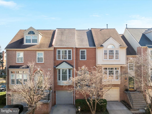 townhome / multi-family property with a garage, roof with shingles, concrete driveway, and brick siding