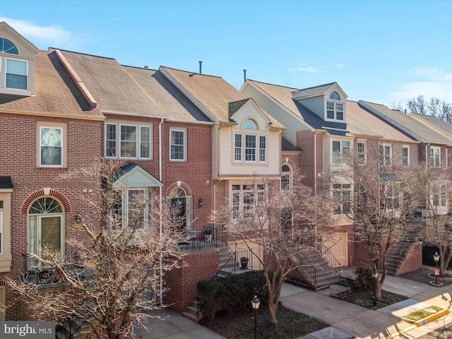 multi unit property with roof with shingles, a residential view, stairway, and brick siding