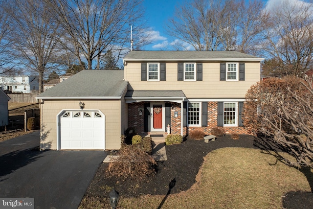 colonial home with an attached garage, roof with shingles, aphalt driveway, and brick siding