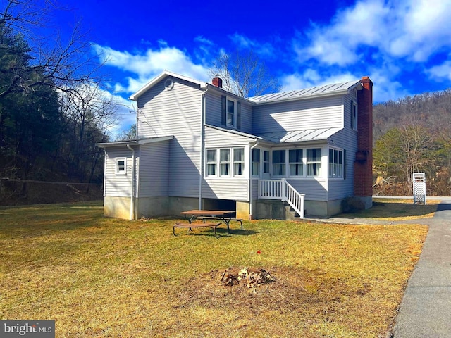 exterior space with a standing seam roof, a chimney, metal roof, and a lawn