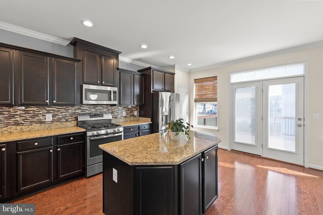 kitchen with light stone countertops, stainless steel appliances, wood finished floors, a kitchen island, and decorative backsplash