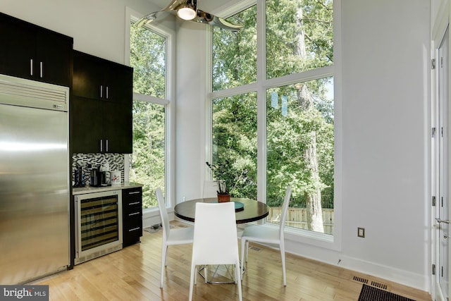 dining area featuring beverage cooler, visible vents, ceiling fan, and light wood finished floors