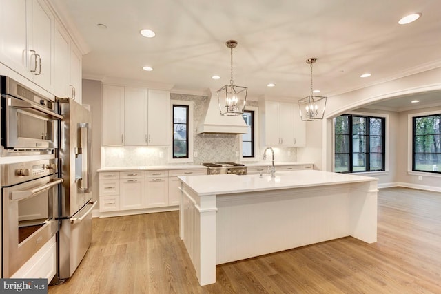 kitchen featuring white cabinetry, light countertops, range, a center island with sink, and custom range hood