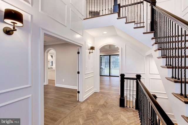 corridor featuring arched walkways, parquet flooring, a towering ceiling, and baseboards