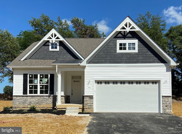 craftsman-style house with a garage, stone siding, and aphalt driveway