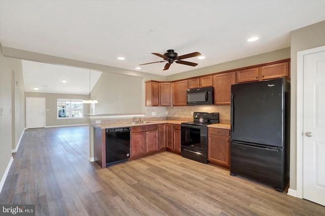 kitchen featuring brown cabinets, light countertops, a peninsula, and black appliances