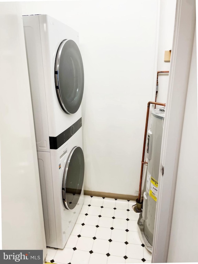 laundry area with light floors, stacked washer and dryer, water heater, laundry area, and baseboards