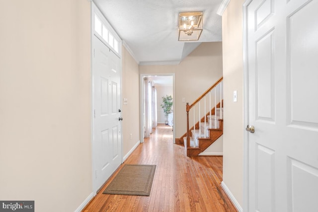 foyer with ornamental molding, light wood-style flooring, baseboards, and stairs