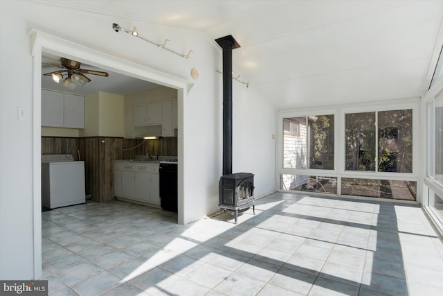 interior space with ceiling fan, light tile patterned flooring, vaulted ceiling, washer / clothes dryer, and a wood stove